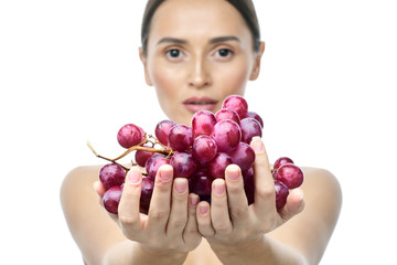 close-up portrait of a girl with clear skin and big brown eyes with soft makeup, with red grapes on a white background