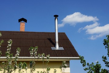 gray metal chimney pipe on a brown slate roof of a house against a blue sky