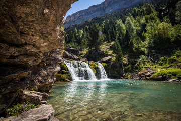 Fototapeta na wymiar Waterfall in crystal clear river with mountains and forest on sunny summer day