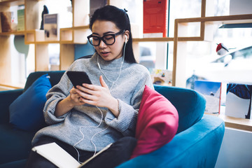 Obraz premium Focused Asian woman sitting on sofa with mobile phone