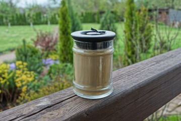 one gray glass jar with a decorative candle stands on a brown board on the veranda against a background of green vegetation