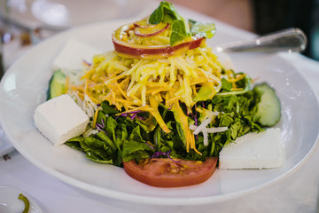 Greek salad with fresh leaves and cheeses on top and feta cheese on a white plate