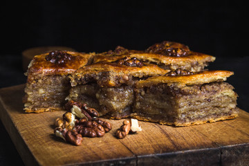 Homemade baklava sliced on a wooden board. Nearby lies a handful of nuts. Photo on a black background