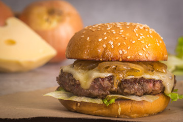 cheeseburger with lettuce and caramelized onion in brown paper on gray background
