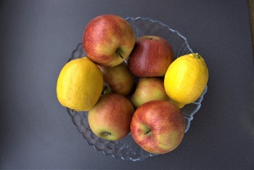 close-up of a bowl full of red apples and yellow lemons on a gray background
