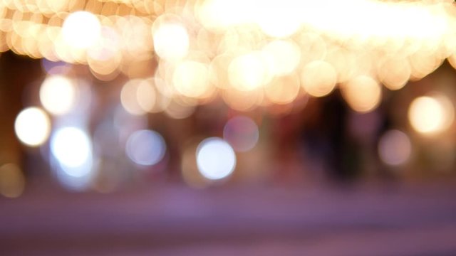 Abstract blurred bokeh background of festival decorative string lights hang and glow outdoors at night with blurrry people moving in festive Christmas market festival.