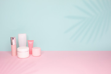 Side view on a still life. Different cosmetic bottles on a bright pink and mint background with palm leaves shadows . 