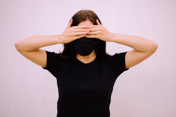 A young brunette girl in a black medical mask and covers her eyes with her hands isolated on white background. Closed up photo. Free space for logo.