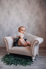 Obraz premium Cute serious newborn baby sitting on sofa. Infant girl sitting on special little baby furniture