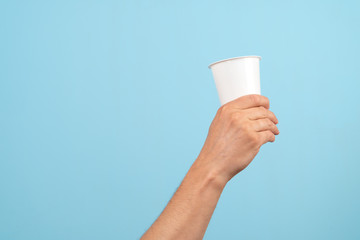 A hand holds a plastic glass on on a blue background. Concept of Recycling and ecology.