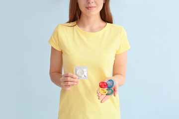 Young woman with condoms on color background