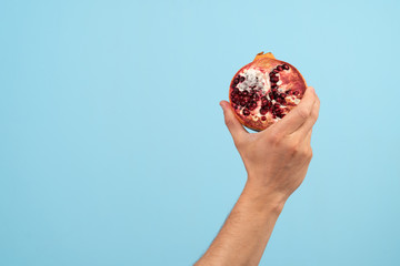 A hand holds a rotten pomegranate organic trash on a blue background. Activist taking care of environment, sorting food waste to proper recycling bin. Concept of Recycling and ecology