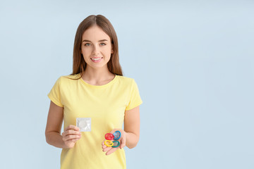 Young woman with condoms on color background
