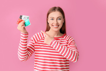 Young woman with condoms on color background