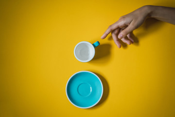 La creación de Adán, mano señalando una taza de café y su plato sobre fondo amarillo minimalista