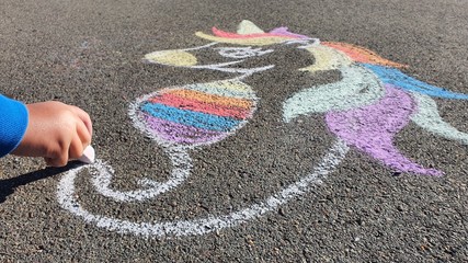 Colourful unicorn child drawing on the asphalt with colourful rainbow chalks