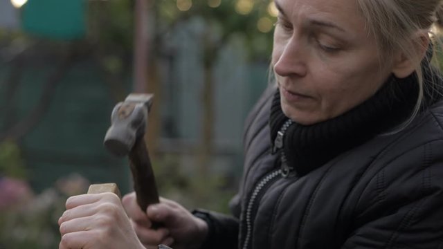 Close-up of an adult woman working with a hammer and chisel on a wooden surface.