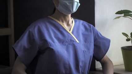 Torso of doctor in blue protective uniform standing near window. Female medical worker in working during coronavirus or covid-19 virus pandemic. Medicine and healthcare concept