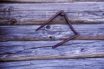 A rusty iron bracket hangs from a nail in a wooden shed.Iron rusty sign on a tree background