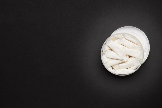 opened container with snus nicotine white bags on a dark background. copy space for design.