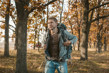 Tourist at the beginning of the journey. An inspired guy with a big backpack got out of a red car and begins his journey through the autumn forest. Hiking concept