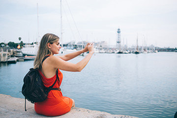 Fototapeta na wymiar Content female tourist taking photo of harbor on smartphone