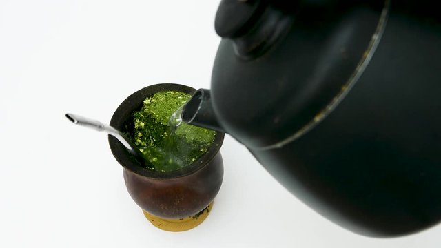 close-up de uma cuia de porongo velha com erva-mate e bomba de inox, recebendo &aacute;gua de uma chaleira para o preparo do chimarr&atilde;o, tradicional no sul do Brasil.