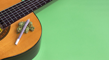 Big marijuana joint and cannabis buds on guitar isolated on green background. Copy space right....