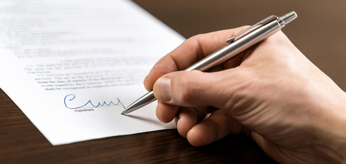 A businessman sits at an office Desk and signs a contract with a ballpoint pen