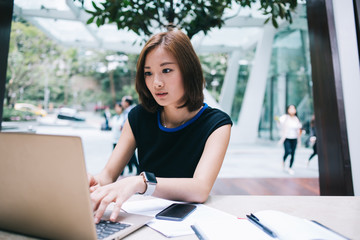 Concentrated Asian female freelancer working on laptop