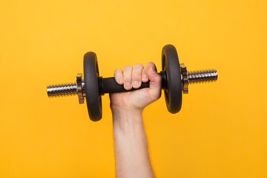 Working out concept. Cropped photo of a strong man holding dumbbell in hand isolated on yellow background