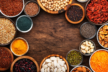 Superfoods, legumes, nuts, seeds and cereals set in bowls on wooden background. Superfood as chia, spirulina, beans, goji berries, quinoa, turmeric, mung bean, buckwheat, lentils, flax seed