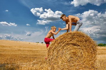 Teenagers in shorts  jump on haystacks. Wheat hay on agricultural field. Children's day. Rural...