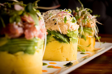 Traditional Peruvian dish called Causa made of mashed potato with aji hot pepper and lime juice and filled with vegetables corn, peas, carrots and mayonnaise Selective Focus, Focus on front