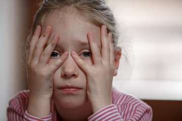 Close up of cute blond hair school girl boring and tired, holding her hand over the face, sad mood, cheerless unhappy kid, closed at home during quarantine 2020
