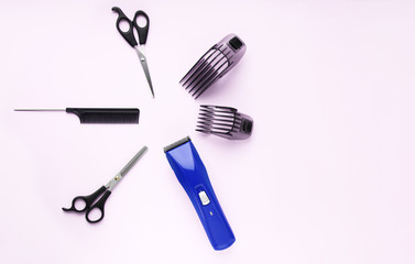 Layout of hairdressing accessories on a pink background.Hairdressing scissors, a comb, and a blue hair clipper with two plastic attachments.Selective focus.Keyboard layout.Space for text. Copy space