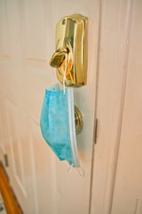 Blue mask hanging from lock as a reminder to wear facemask when leaving home to protect face, nose, and mouth from coronavirus