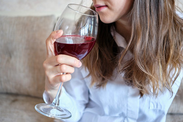 Drunk girl drinks wine from a glass on the couch.