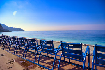 Fototapeta na wymiar Blue chairs along the Promenade des Anglais on the Mediterranean Sea at Nice, France along the French Riviera.