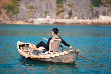 Fisherman sitting on plastic chair and rowing with legs fishing
