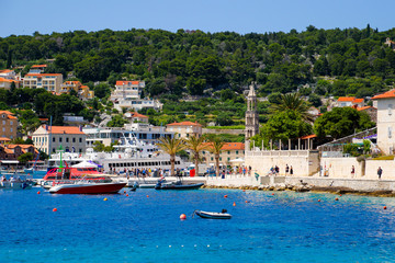 Hvar harbor from the distance with tourists swimming in the Adriatic Sea in Croatia - Hill covered with tile-roofed cottages