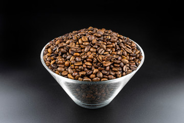 Fresh, roasted coffee beans in a glass bowl, standing on a black table.