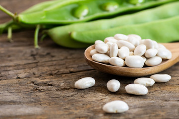Uncooked dried white haricot beans in wooden spoon with fresh raw green beans pod plant on rustic table. Heap of legume haricot bean background ( Phaseolus vulgaris )