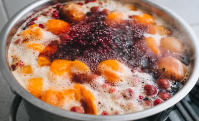 Fresh fruits are boiled in boiling water in a metal pan on the stove. Delicious stewed apricot, apples, cherries, raspberries. Photography, concept.