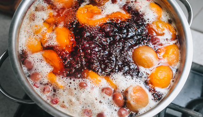Fresh fruits are boiled in boiling water in a metal pan on a stove with bubbles and foam close-up. Cooking a delicious compote of apricot, apples, cherries, raspberries. Photography, concept.