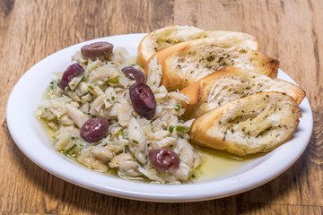 shredded cod with olive oil and olives served with bread toast on wooden background