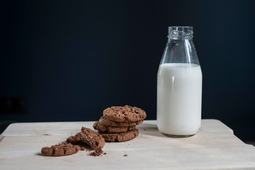 Bottle of milk with oatmeal cookies on a background of a dark blue wall on a white vintage wooden chair.