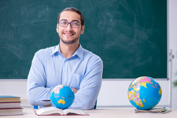 Young male geography teacher in front of blackboard