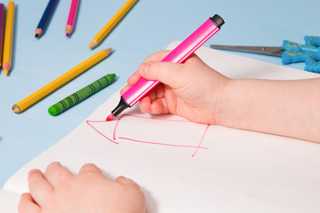 a small child painstakingly paints with a pink felt-tip pen a house in an album, a copy place, a top view, a blue background, what to do with a quarantined child, activities for children