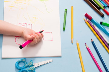a small child painstakingly draws with a pink felt-tip pen in an album, copy space, top view, blue background, what to do with quarantine, activities for children at home